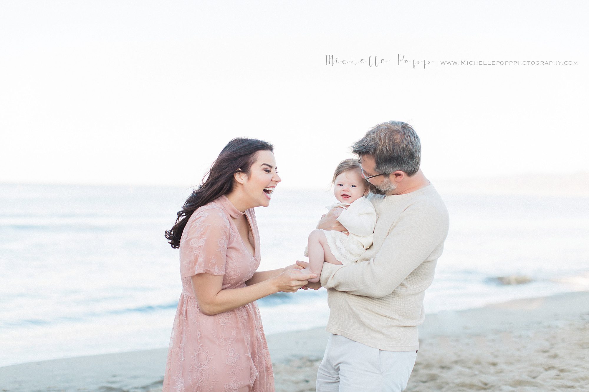 Mom and dad smiling at baby girl on the beach