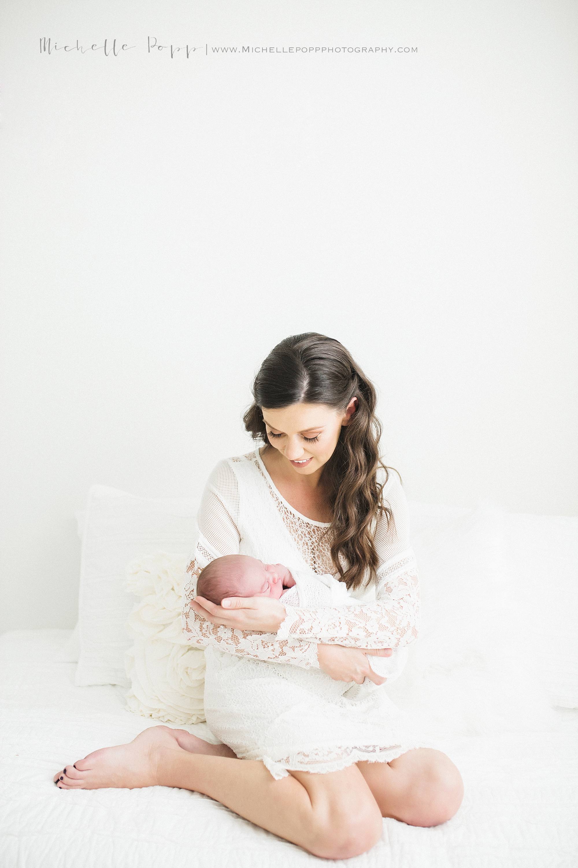 Mom in all white lace dress holding newborn baby 