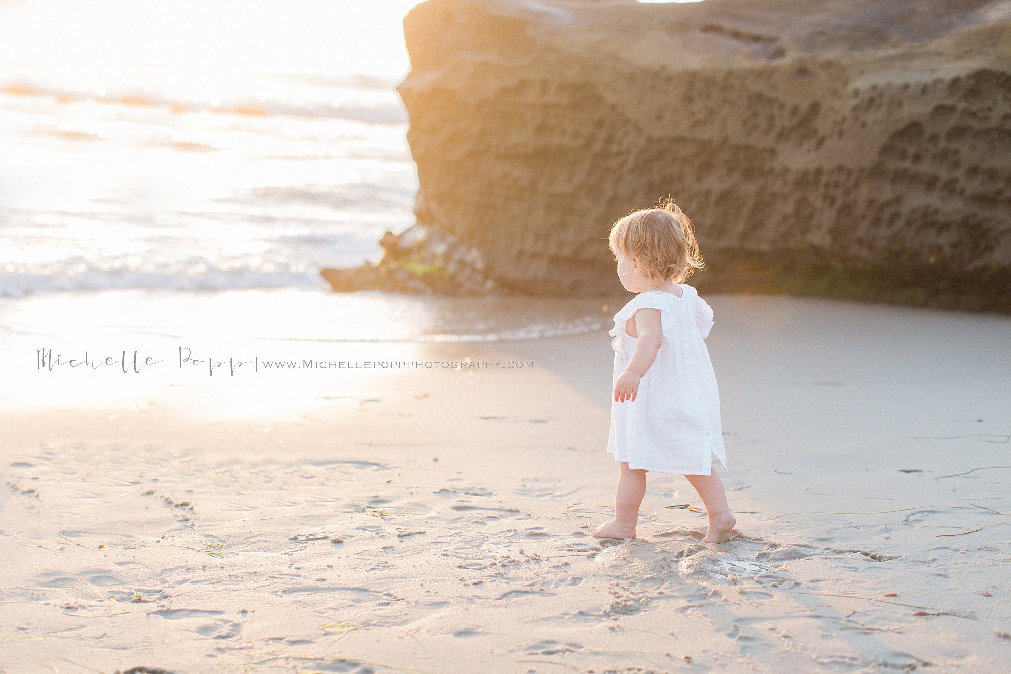 baby girl walking on the sand towards the ocean