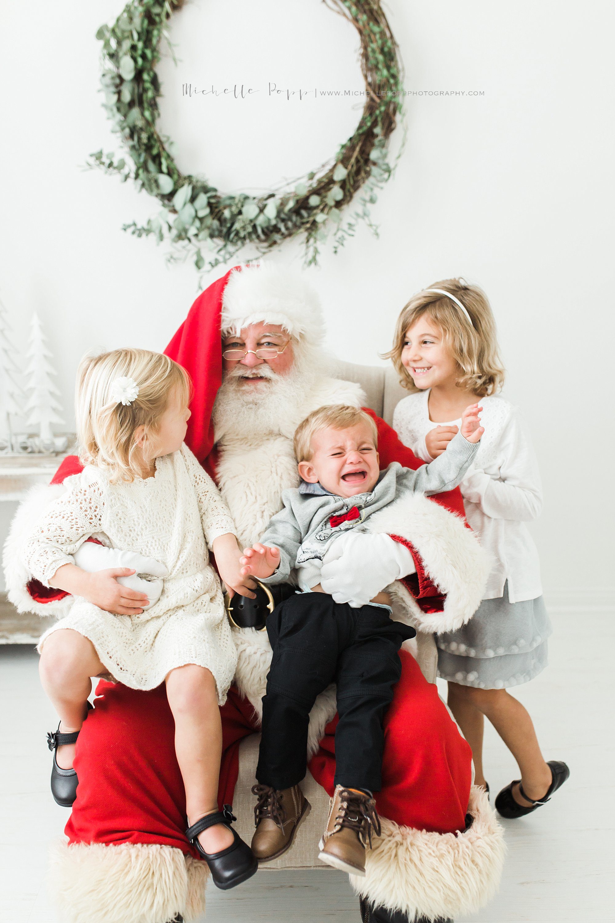 three siblings on Santa's lap with little boy crying