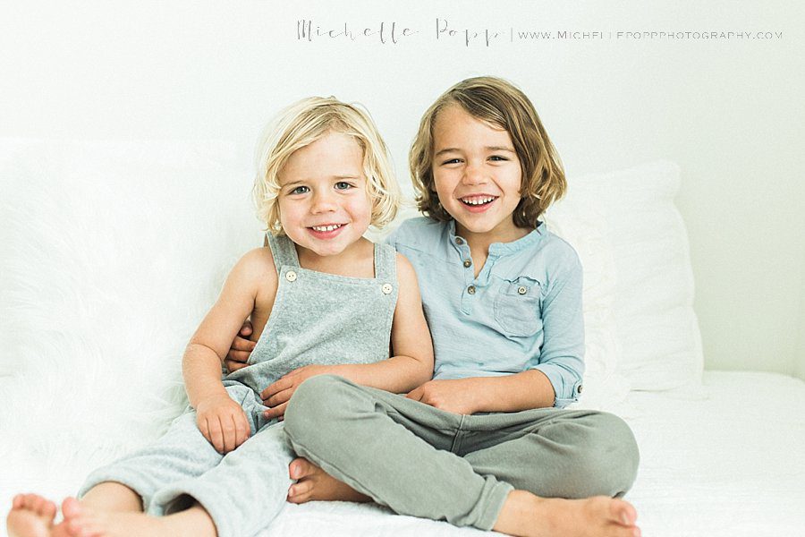 toddler brothers sitting on bed smiling 