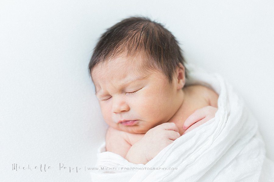 close up of newborn baby in white swaddle 