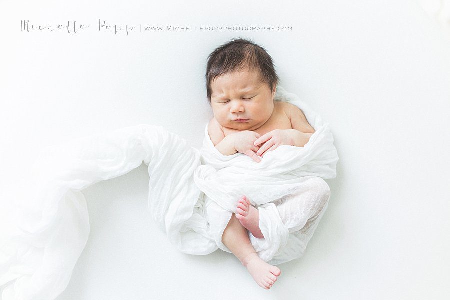newborn baby girl in white swaddle blanket