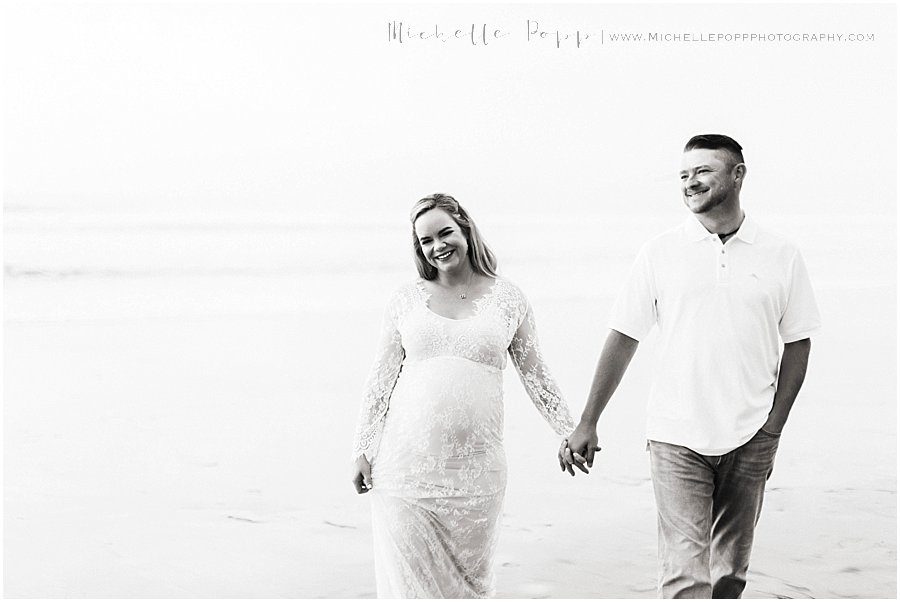 maternity session with couple walking hand in hand on beach