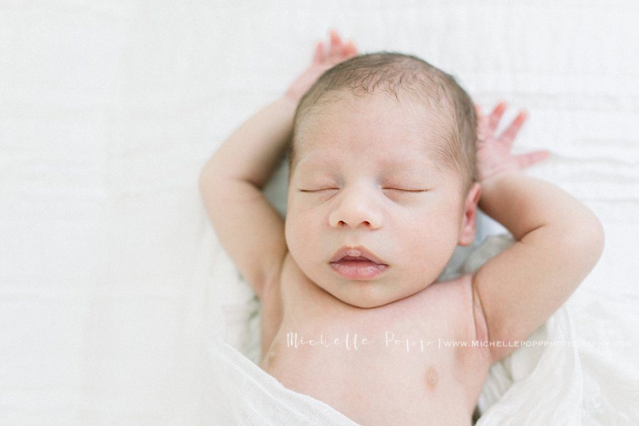 beautiful newborn baby stretches as he sleeps in a cozy bed during a newborn portrait session