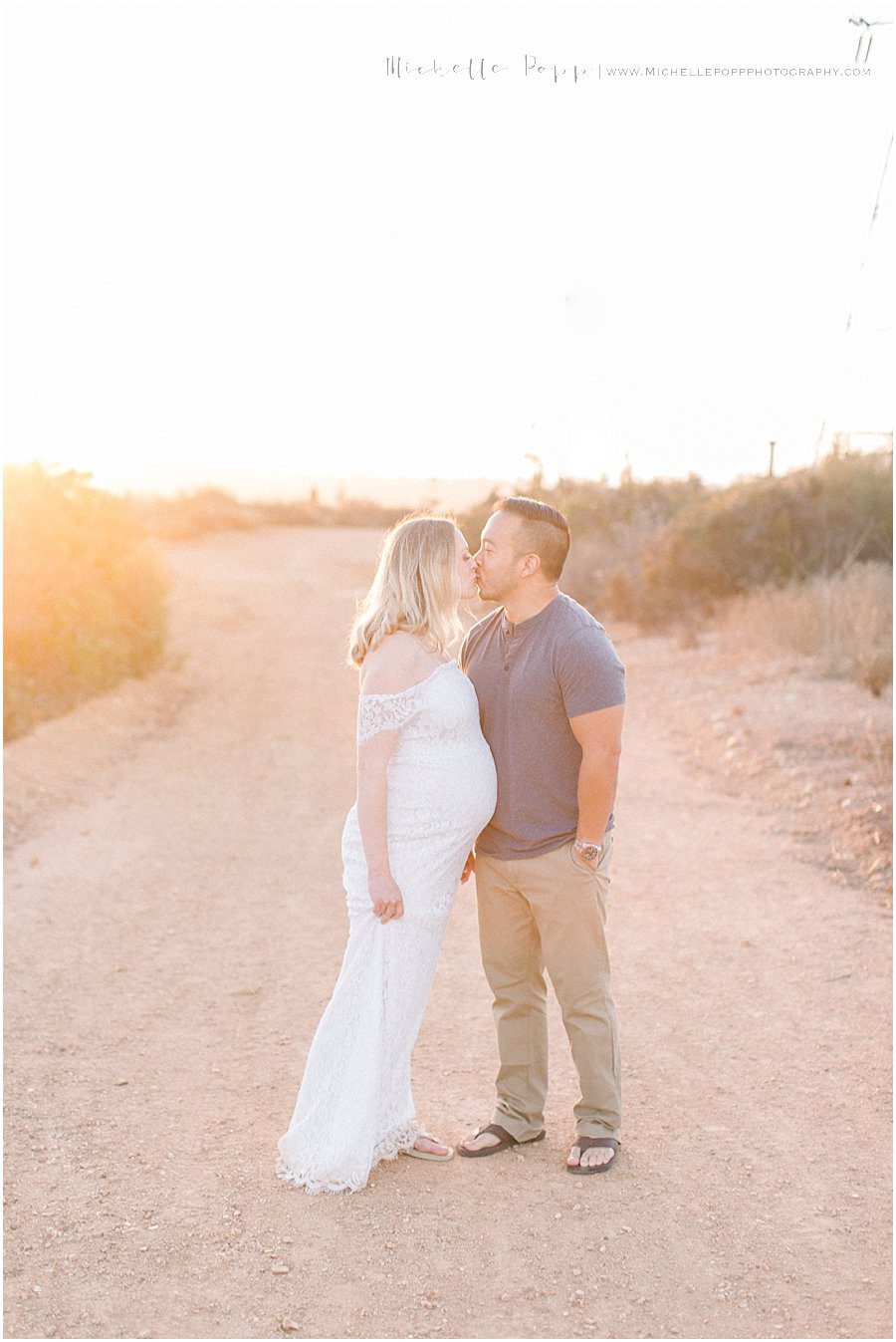 a husband and wife kiss as the sun sets behind them during their maternity photo shoot
