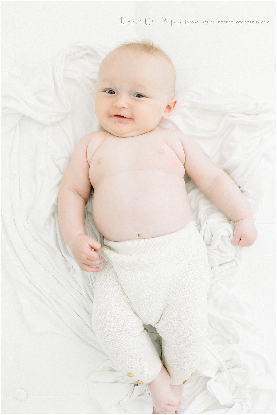 smiling baby boy lying on sheets during baby photography session