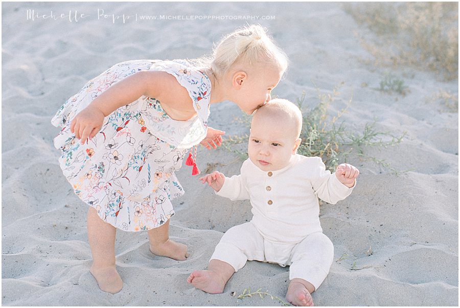 young girl kissing her baby sibling's forehead during a beach photo shoot