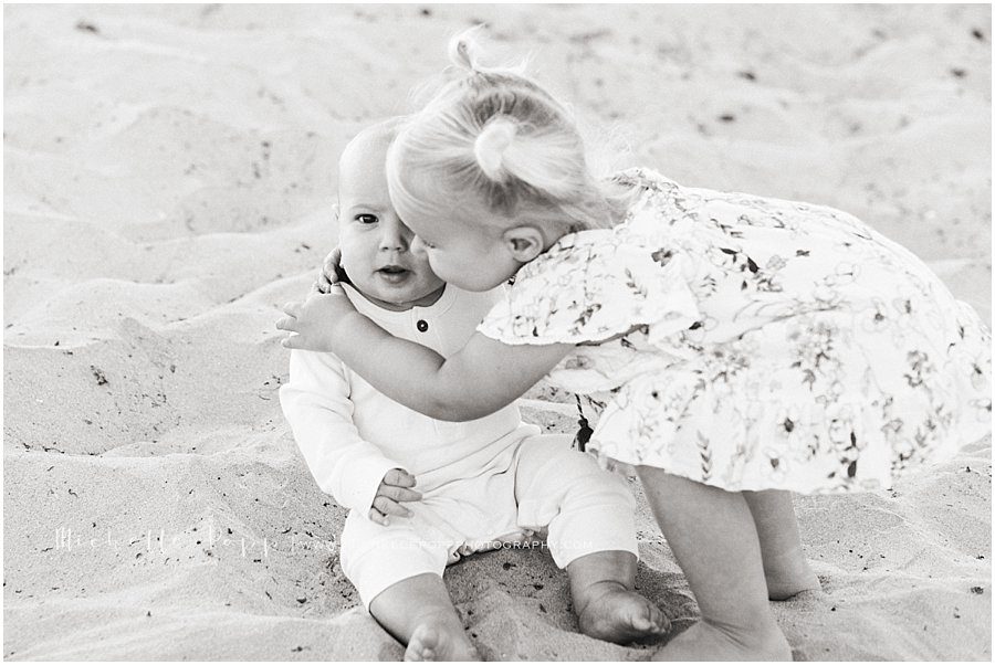 young girl hugging her baby sibling in the sand on the beach