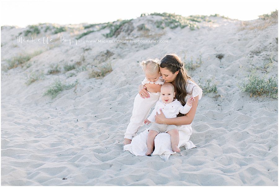 mother holding her two children close while sitting on the beach