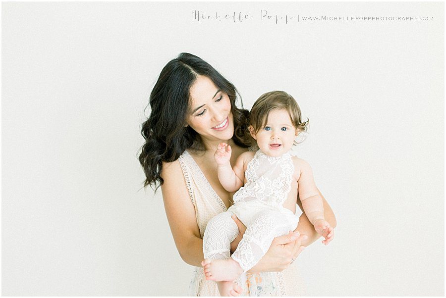 a baby girl and her mother smile and look at the camera during a natural baby photography session