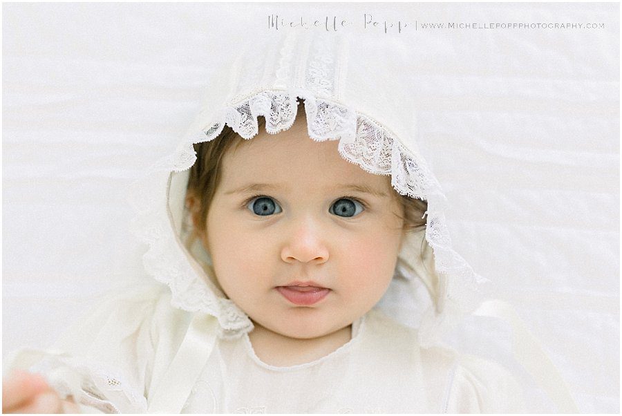 a baby girl wearing a white hat looks curiously at the camera during her natural baby photography session