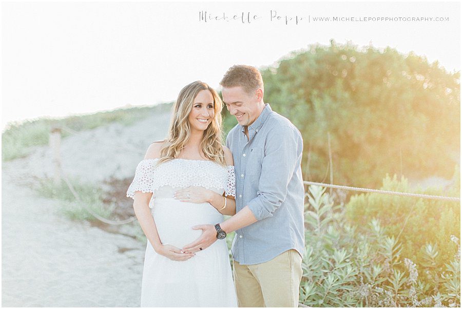 husband and wife smiling on a beach during their maternity photography session