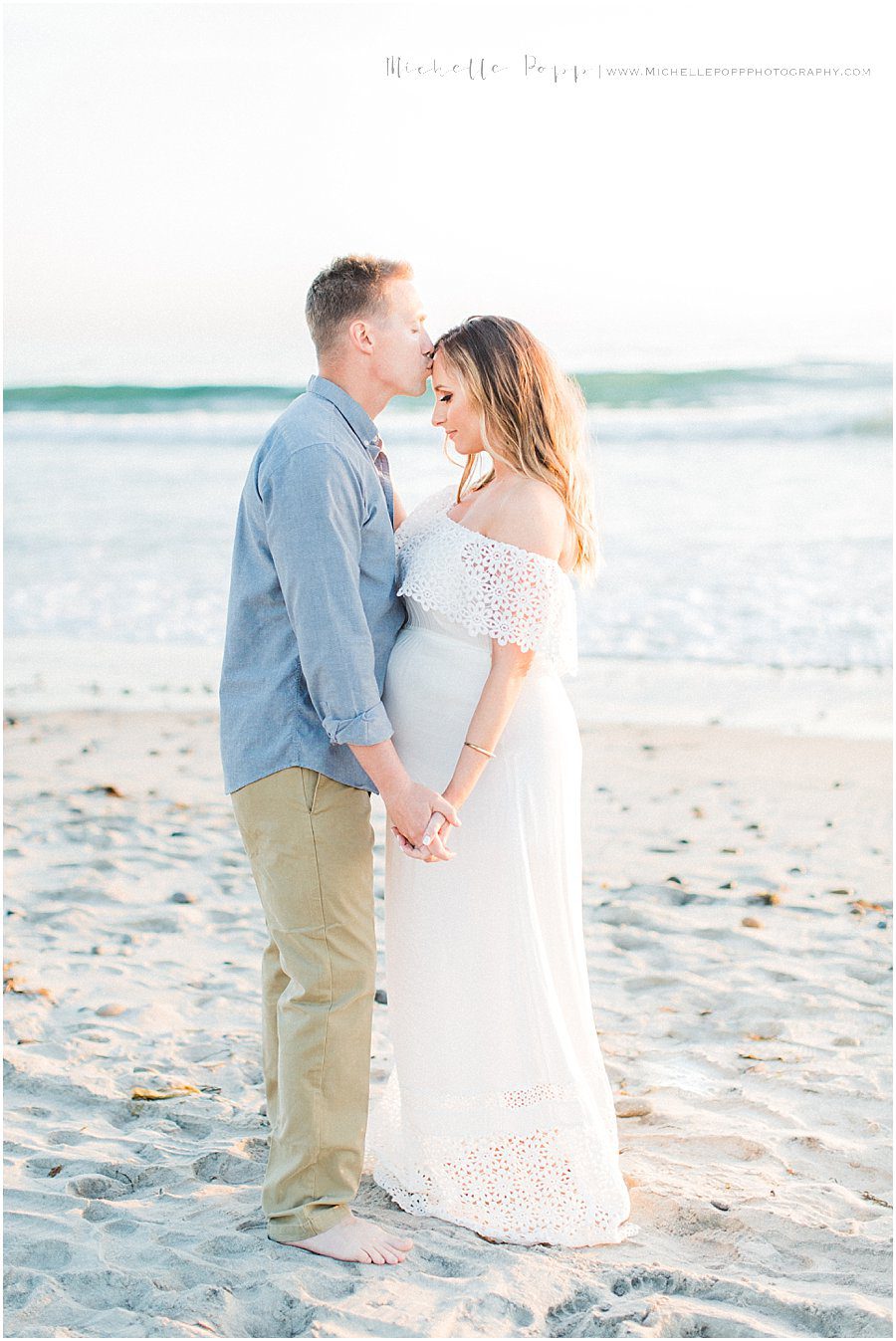 husband kissing his wife's forehead while they stand on a Carlsbad beach