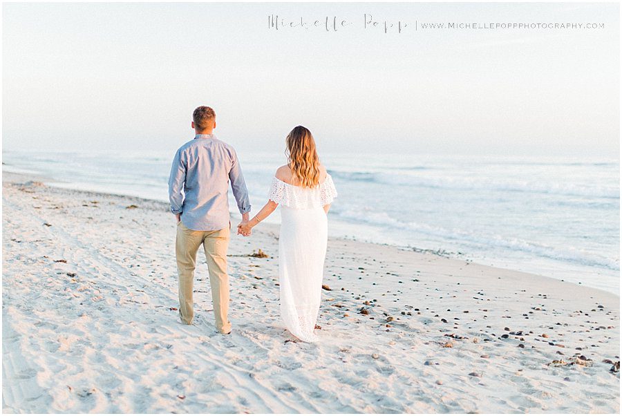 husband and wife holding hands on a beach during their maternity photography session
