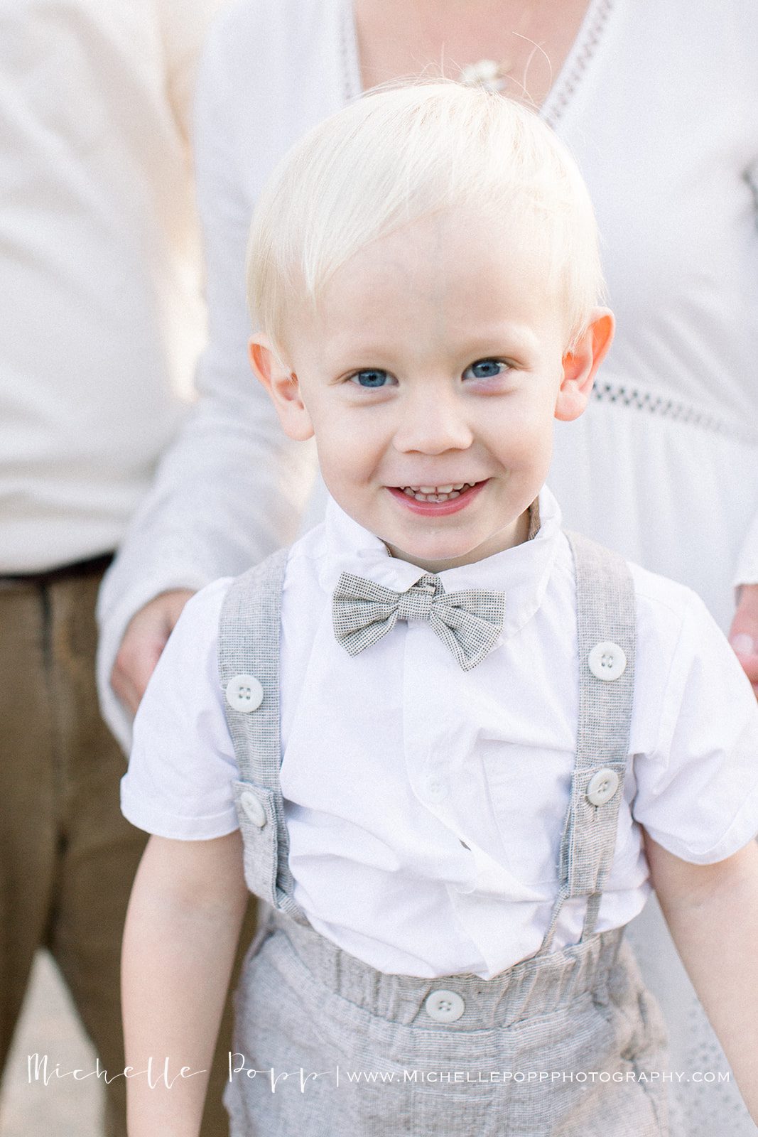little boy smiling wearing a bow tie and grey neutral trousers for family photo session in san diego