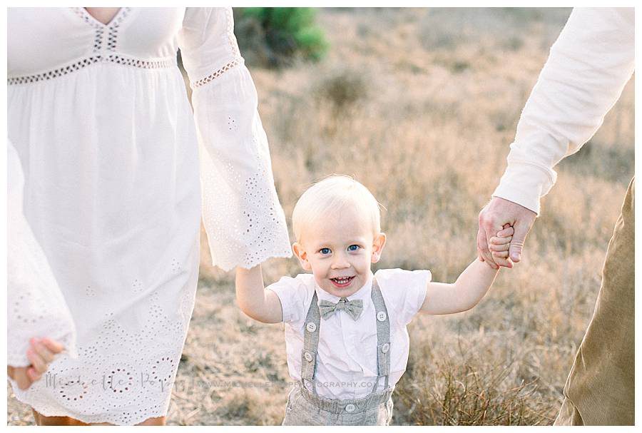 mom and dad holding smiling little boys hands