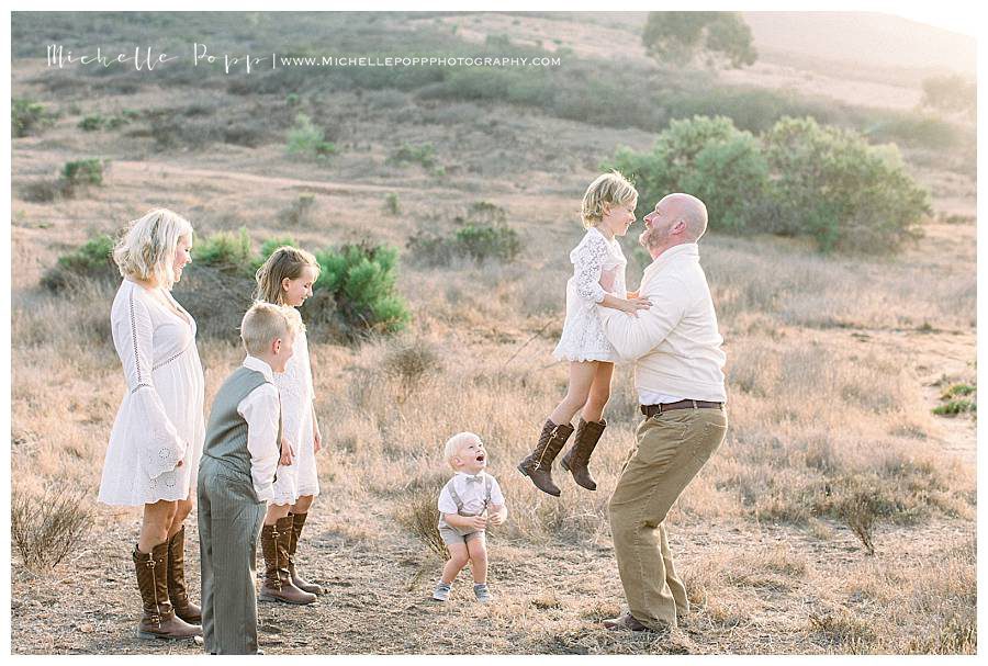 dad lifting up daughter into air while family watches and laughs