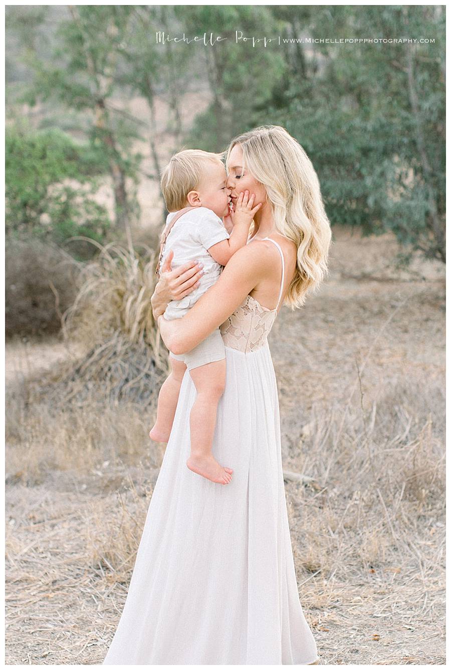 mom kissing baby boy in field