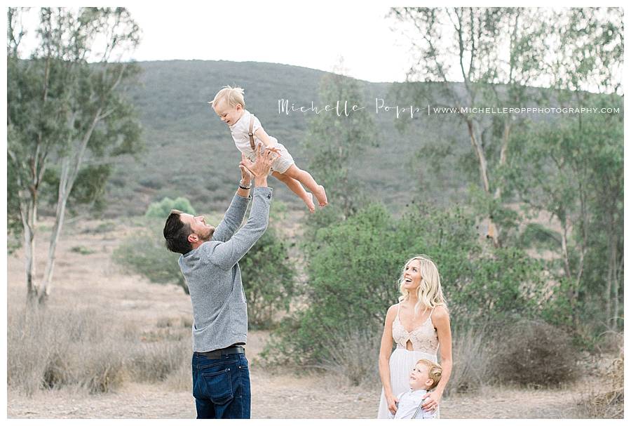 dad throwing son into air while family watches smiling