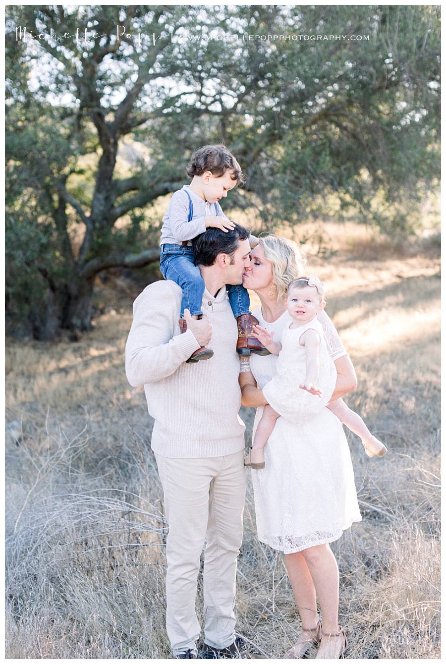 mom and dad kissing with kids on shoulders