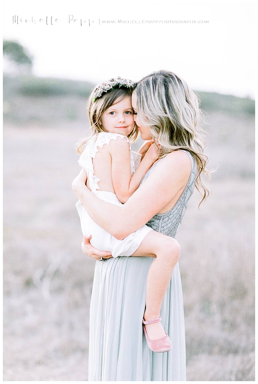 mom holding daughter while daughter looks at camera