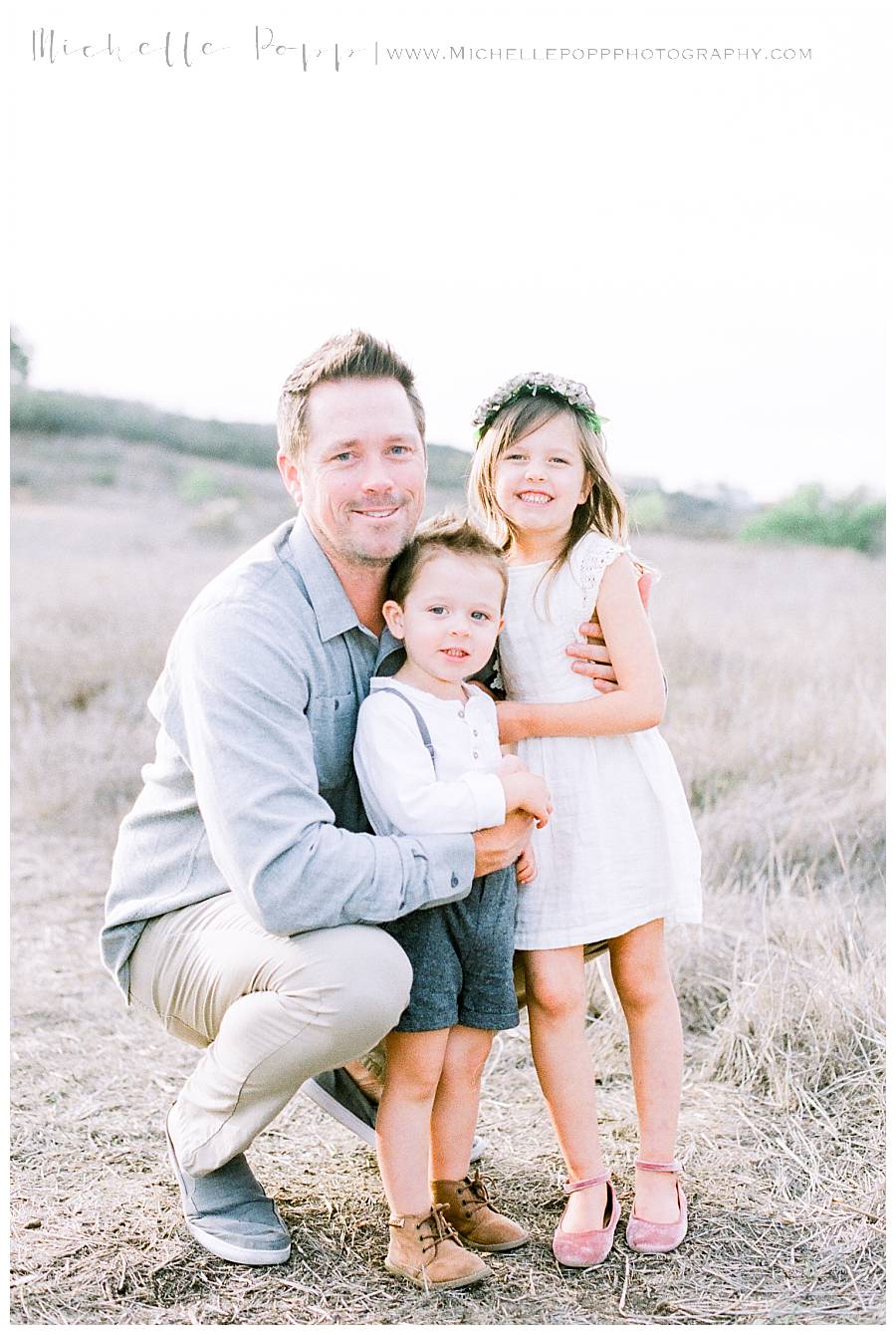 dad holding two kids in field and smiling