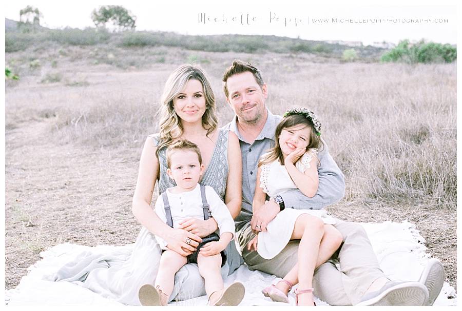 family of four sitting on blanket in field