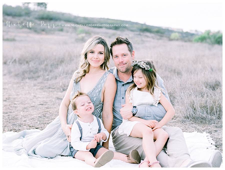 family of four sitting on a blanket in field