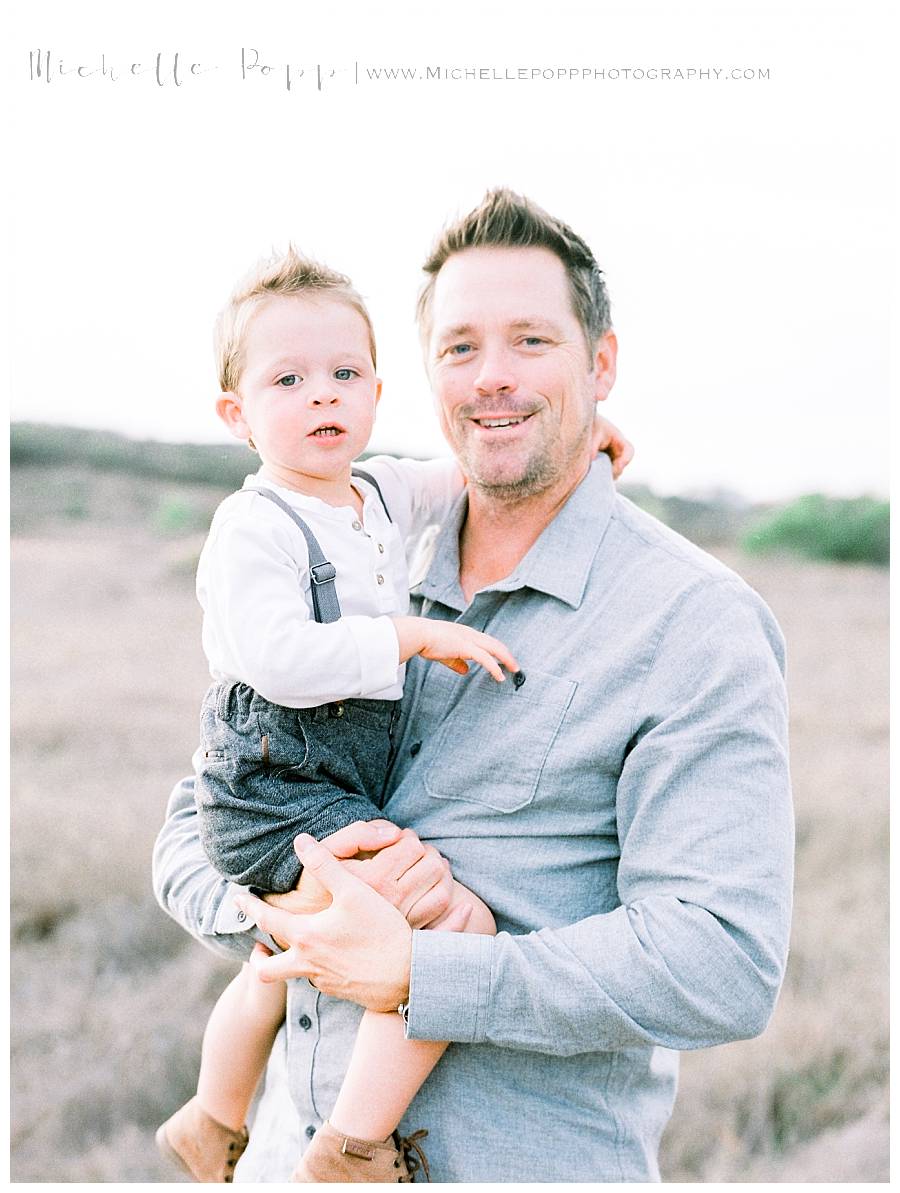 dad holding baby boy in arms in field