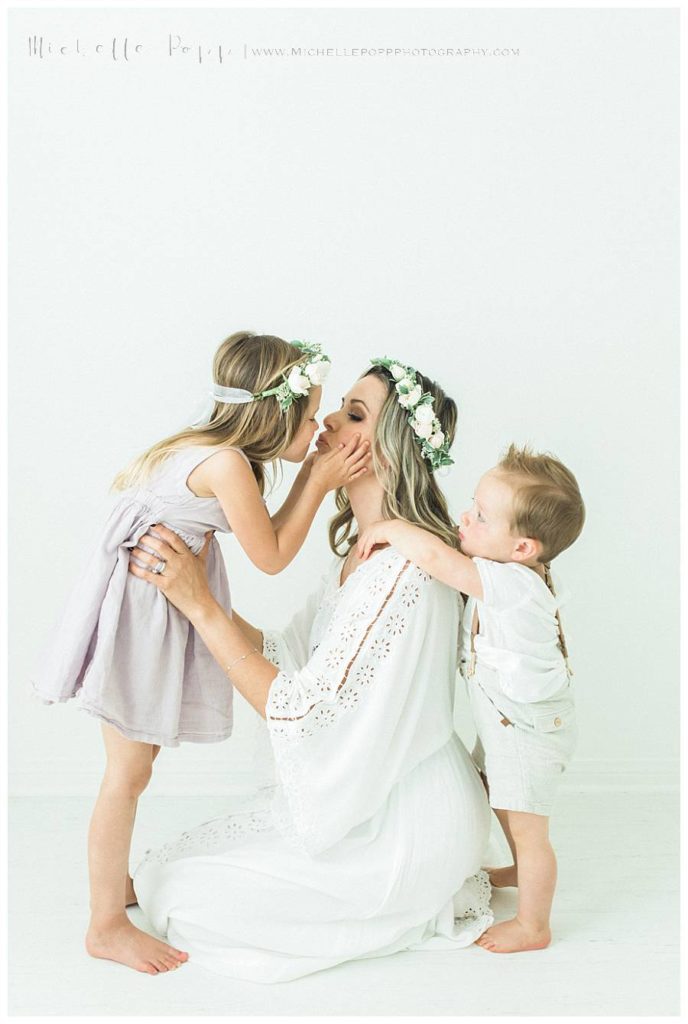 mom kissing littl girl with baby brother