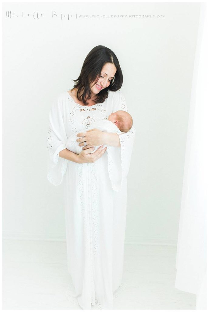 mom in white dress smiling down at new baby