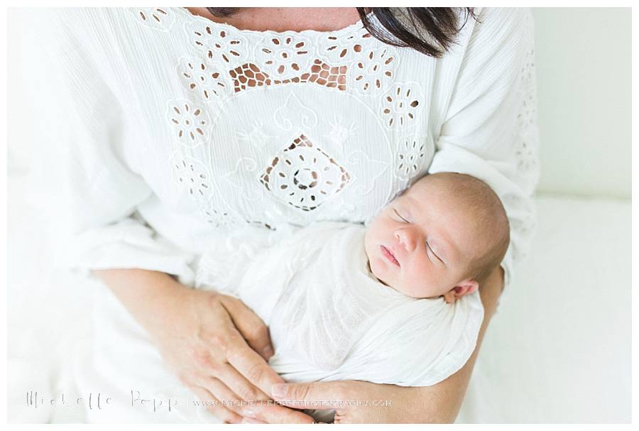 close up of newborn baby in white swaddle in moms arms