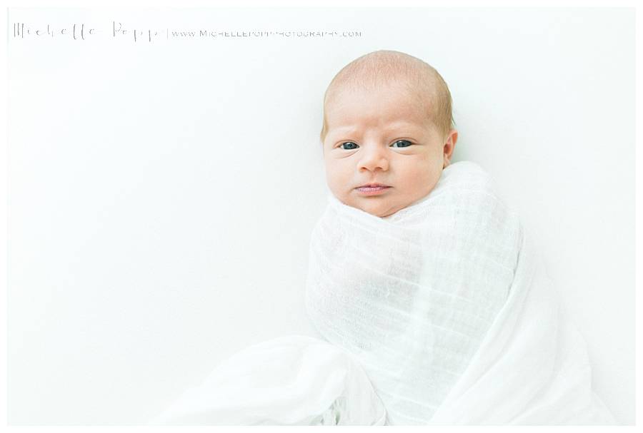 newborn baby eyes open in white swaddle