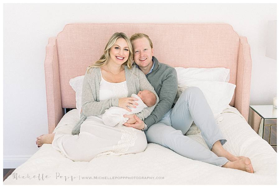mom and dad holding newborn baby girl on pink bed