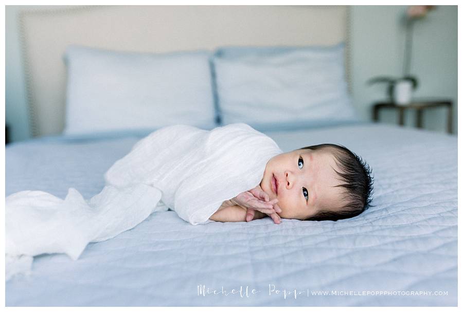 newborn baby girl on bed in white swaddle