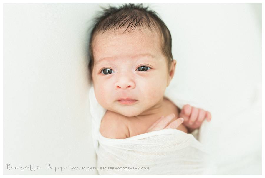 newborn baby with eyes open on white bed