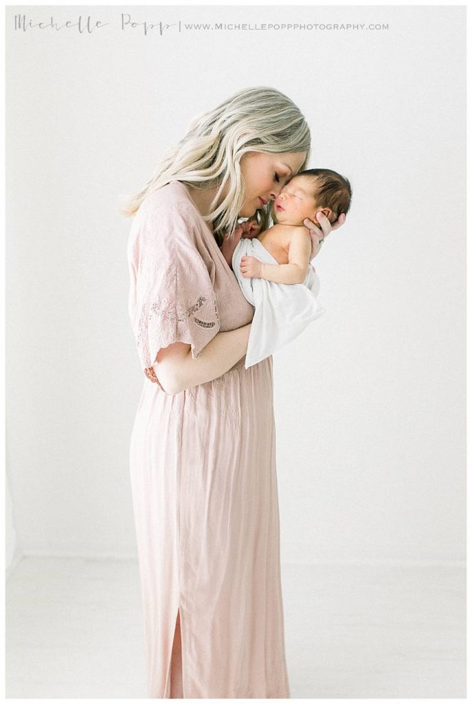 mom in pink dress holding baby boy in white swaddle