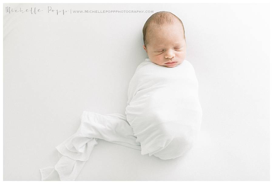 newborn baby on bed in white swaddle