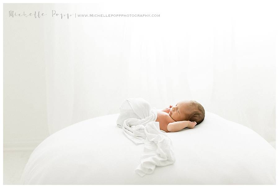 newborn baby on bed in white swaddle