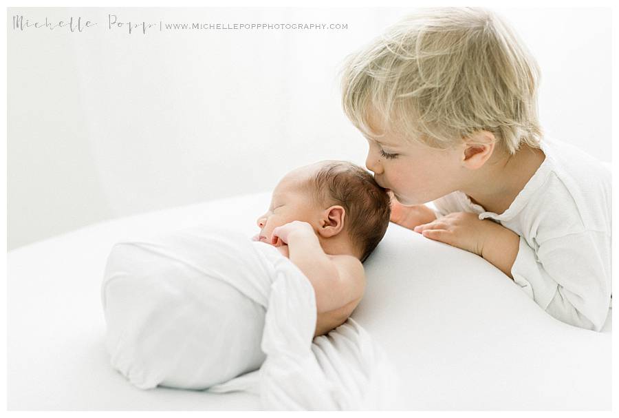 big brother kissing newborn baby on head