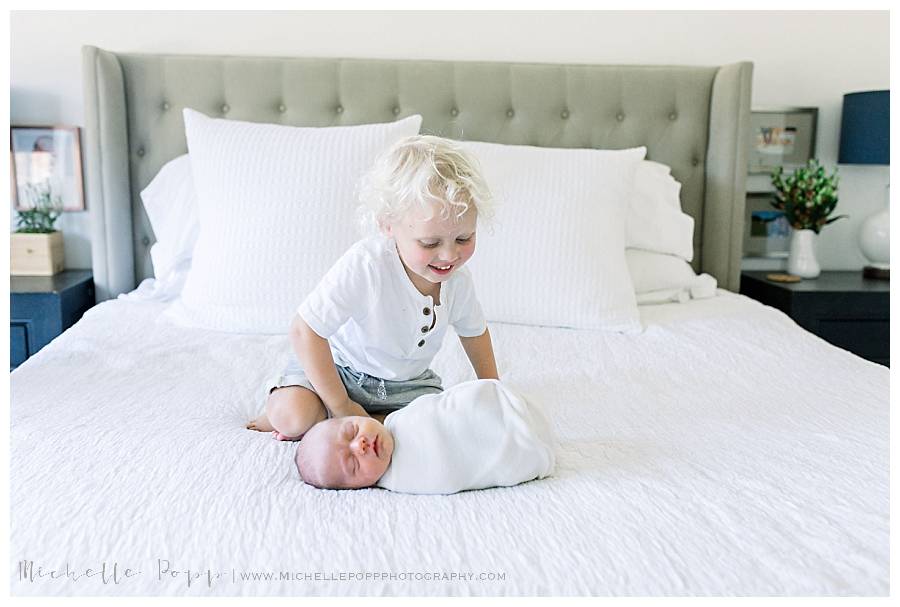 big brother looking at newborn brother on bed