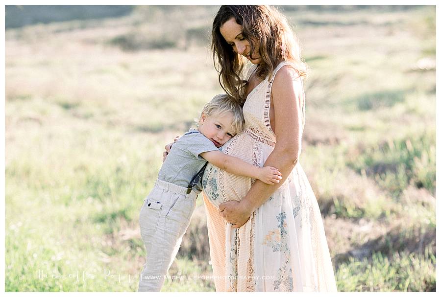 son hugging mom's belly in field