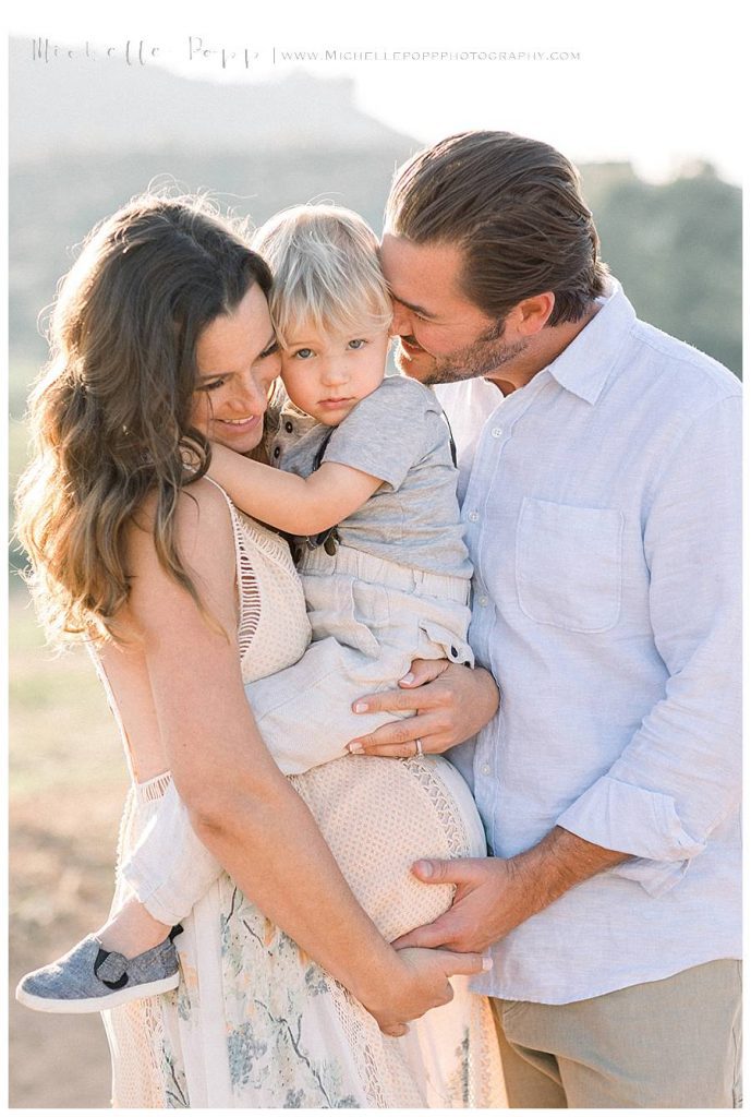 mom and dad snuggling baby boy in field