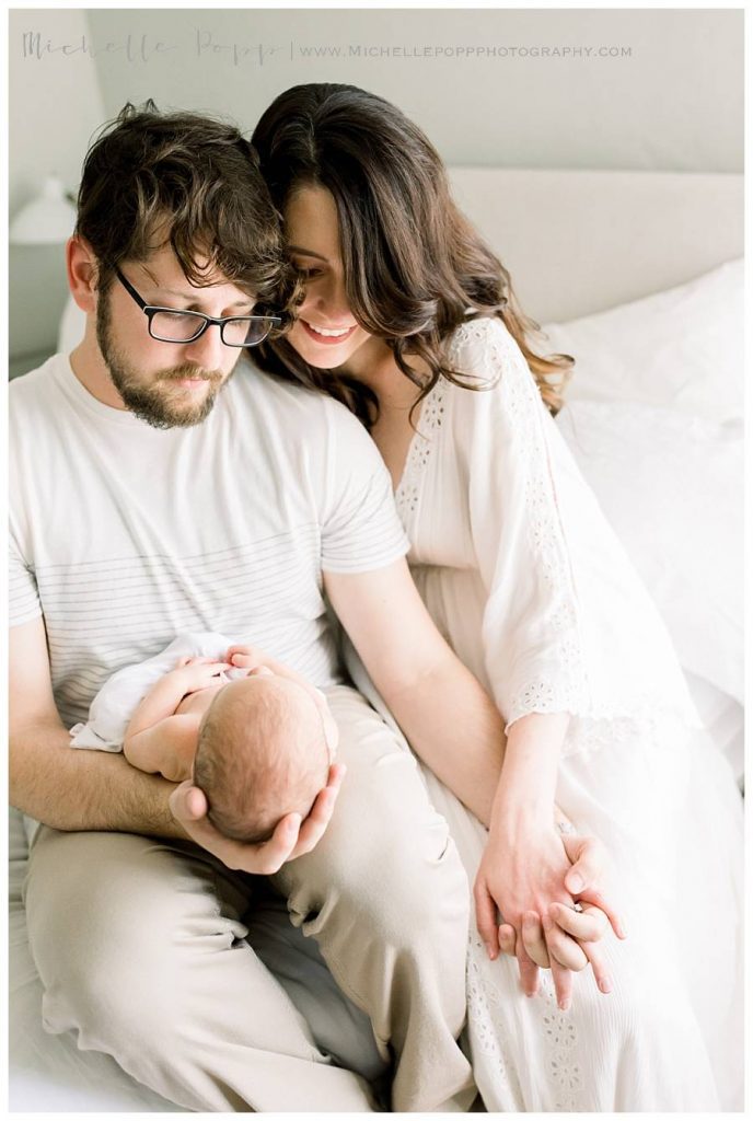 mom and dad holding baby on bed