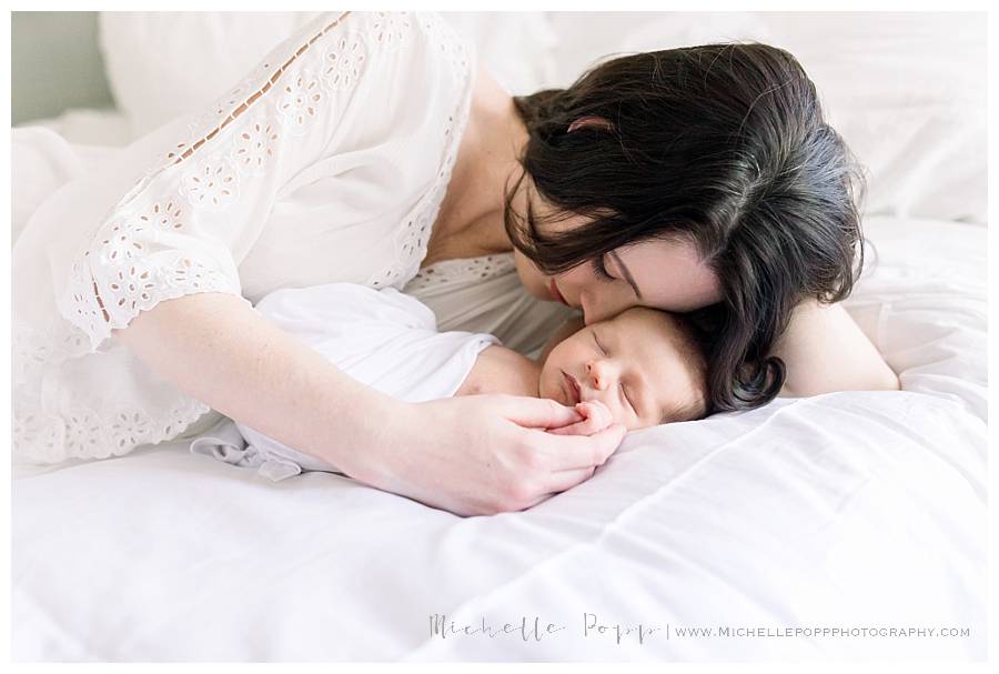 mom snuggling newborn baby on bed