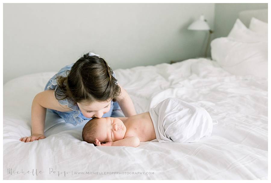 sister kissing newborn baby on head