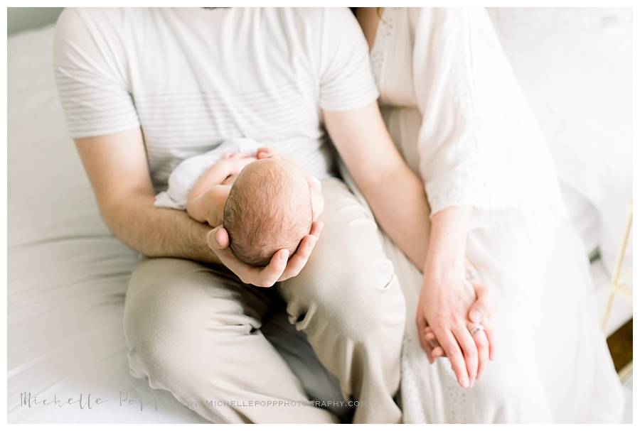 mom and dad sitting on bed holding newborn