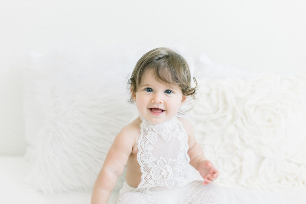 baby sitting up in bed in white dress