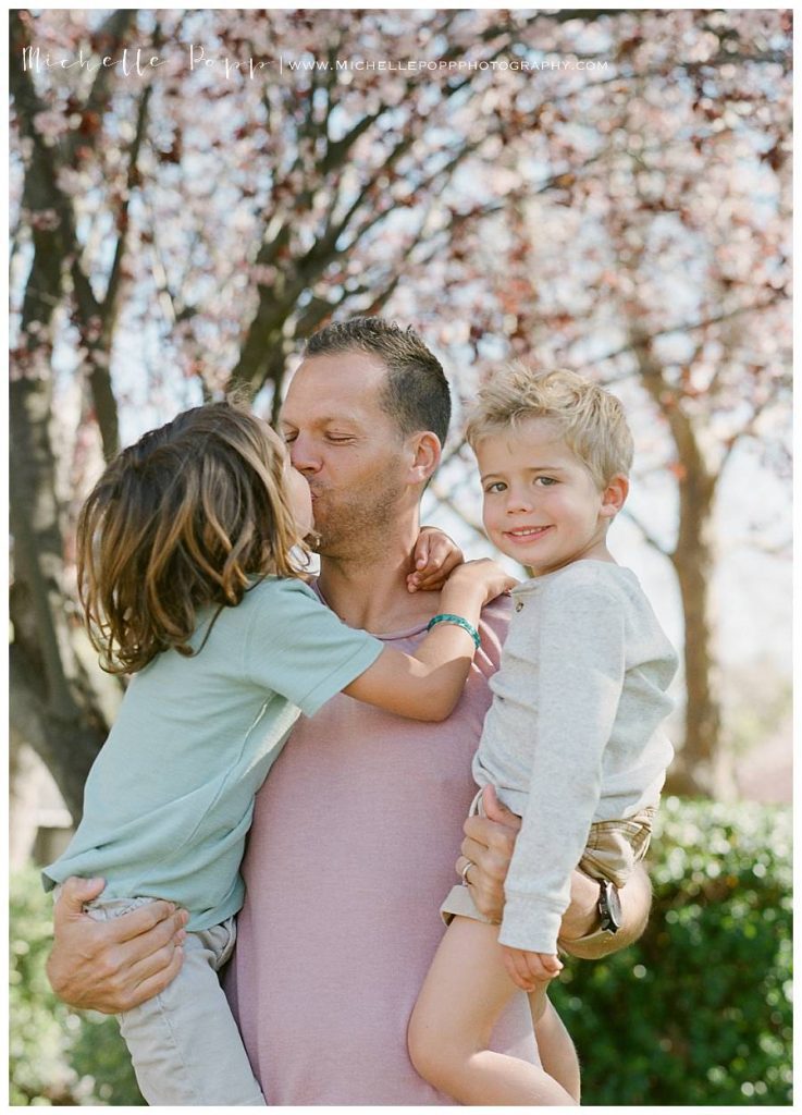 dad holding two sons under a tree